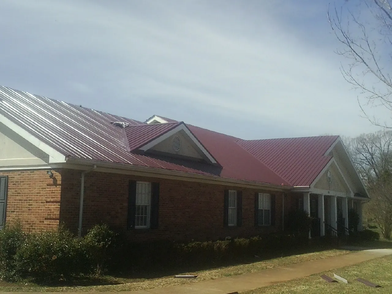 Red metal roof with gabled entries on a long brick building, from a Hail Damage Roof Repair job in Robeline