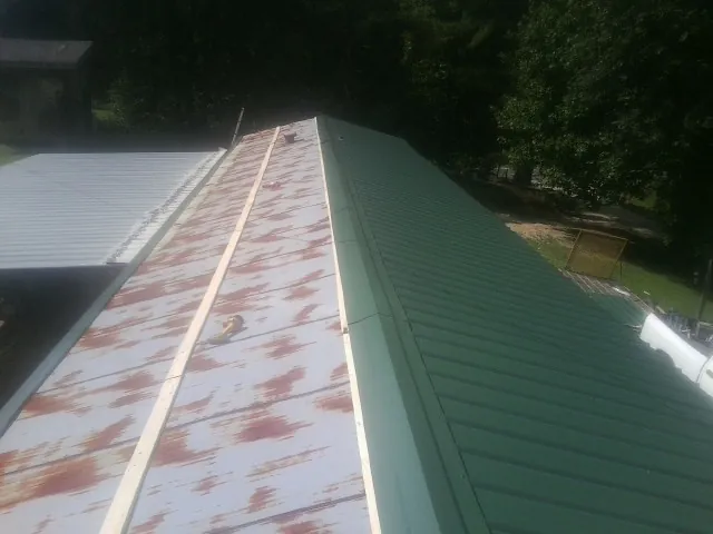 Old rusted panels beside newly installed green metal roofing — Wind Damage Roof Repair by Roofing Brothers in Robeline