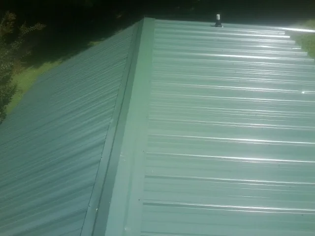 New green metal panels meeting at the ridge of a roof — Flat Roof Repair work by our crew in Robeline