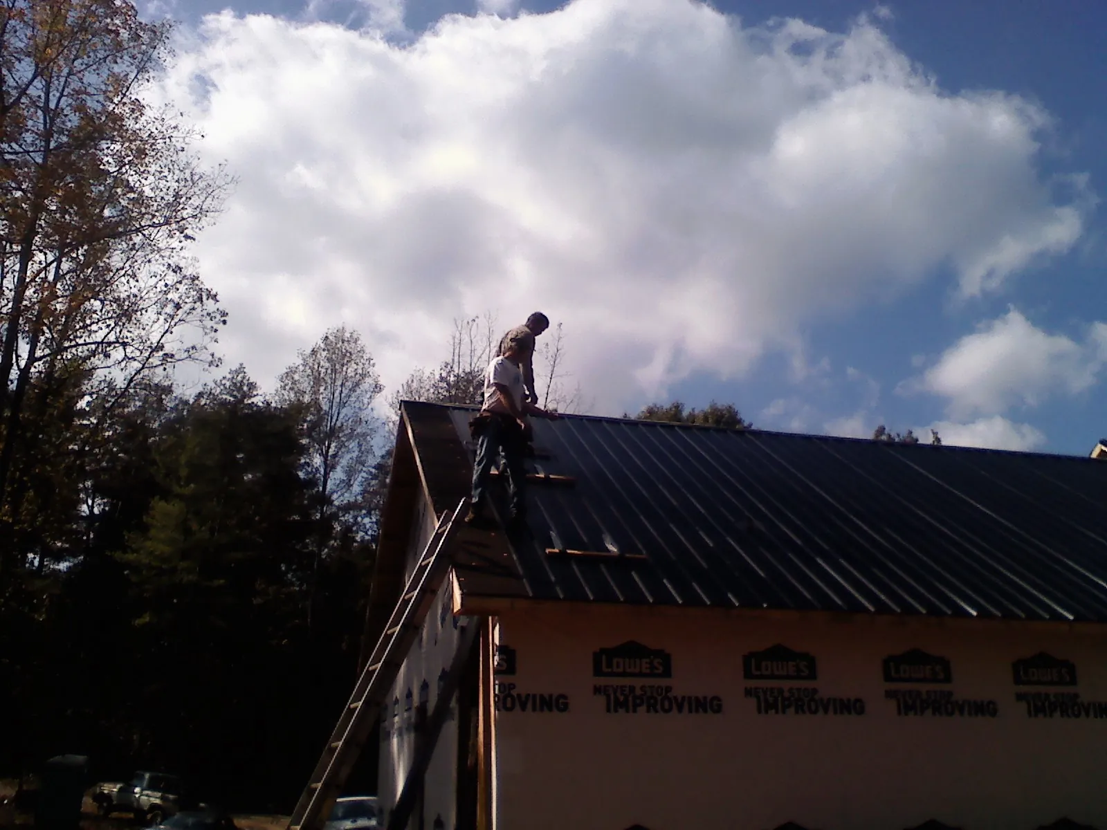 Roofer fastening dark metal panels high against a cloudy sky, from a Roof Inspection job in Robeline