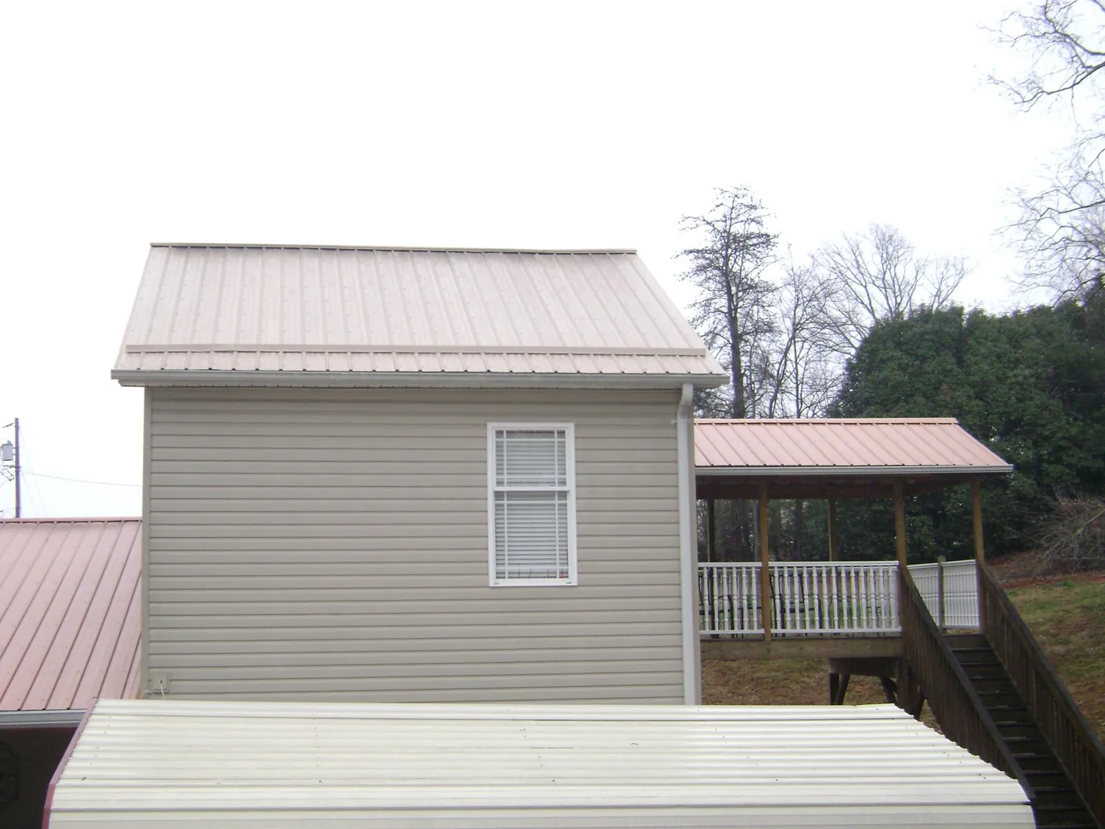 Tan metal roofs on a two story addition and attached porch, from a Roof Replacement job in Robeline
