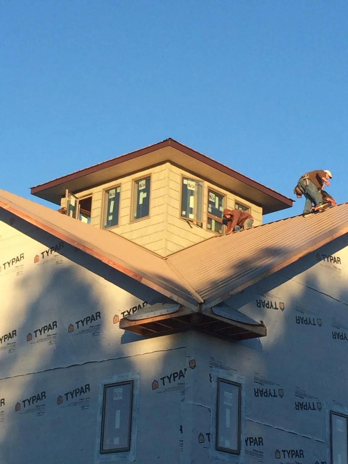 Roofers working around a rooftop cupola on a new metal roof at sunset — Roof Waterproofing in Robeline by Roofing Brothers